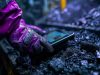 A miner's gloved hand interacts with a smart device among coal chunks