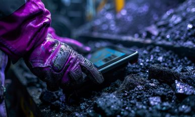 A miner's gloved hand interacts with a smart device among coal chunks